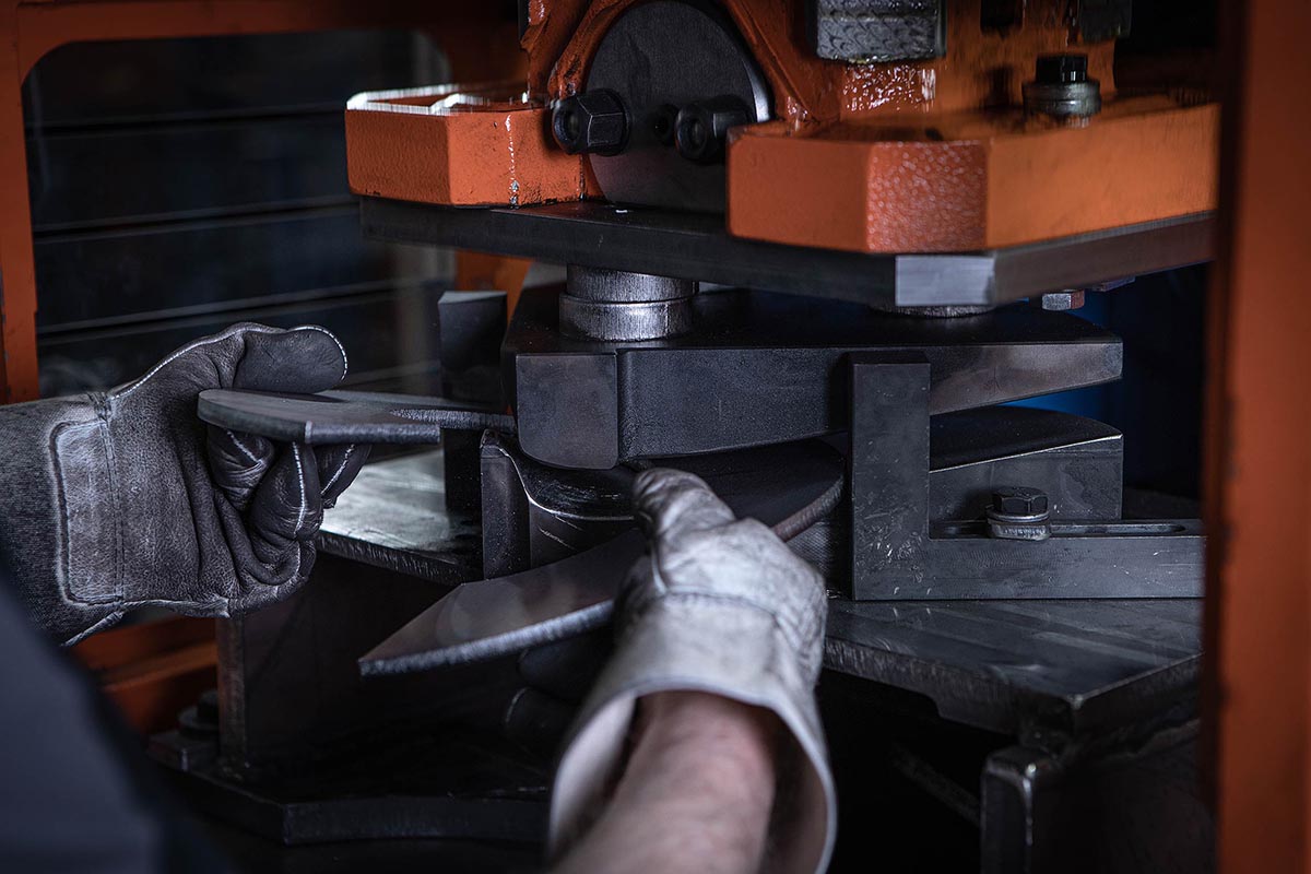 Hände eines Mitarbeiters die ein Stück Metall in der Hydraulikpresse halten